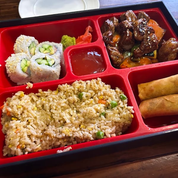 A bento box with sushi, beef and vegetables, fried rice, and egg rolls.