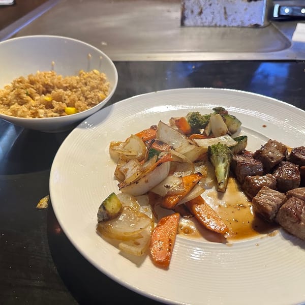 Hibachi steak, mixed vegetables, and fried rice served on a dark table with a grill in the background.